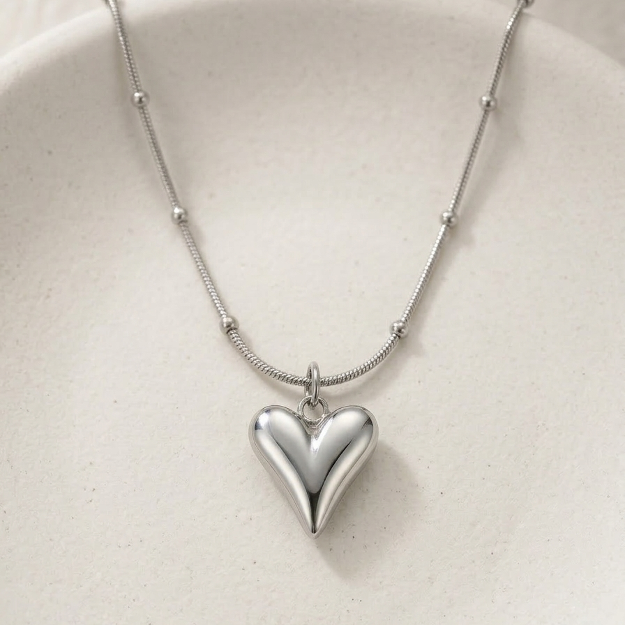 Silver-tone rhodium plated necklace featuring a smooth, 3D puffy heart pendant suspended on a delicate beaded satellite chain.