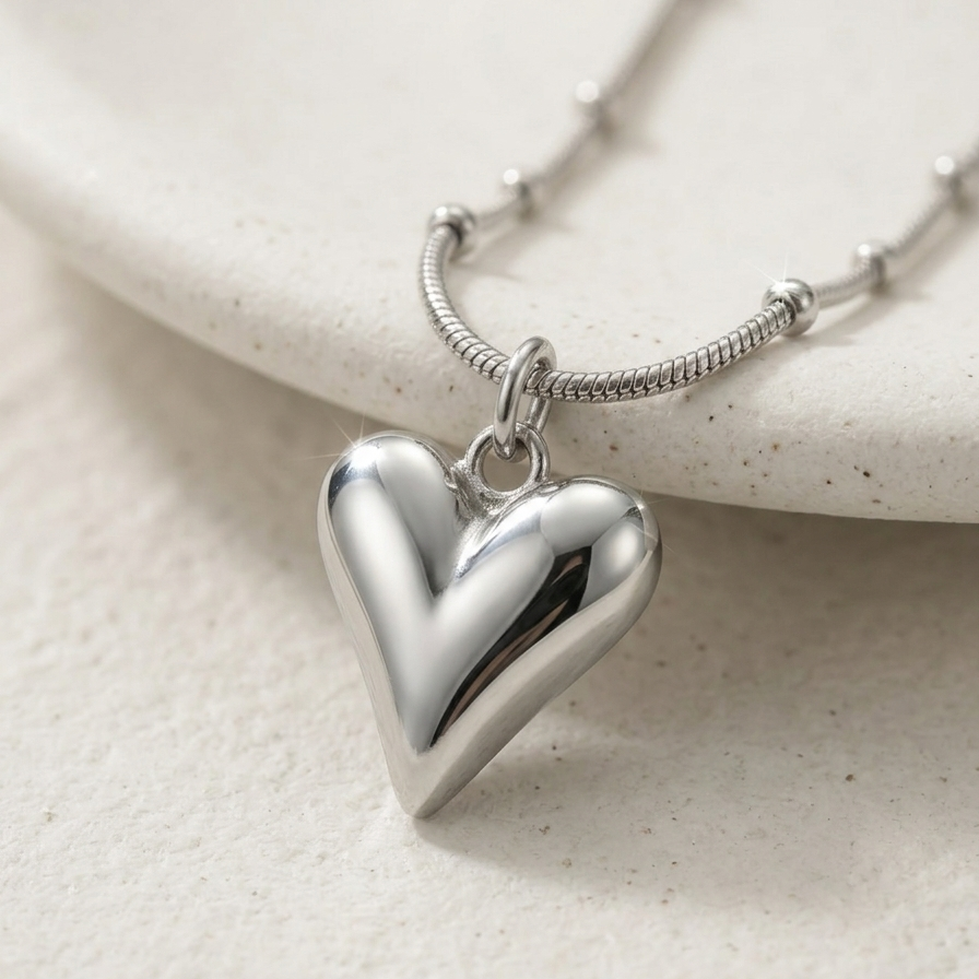Close up of a Silver-tone rhodium plated necklace featuring a smooth, 3D puffy heart pendant suspended on a delicate beaded satellite chain.