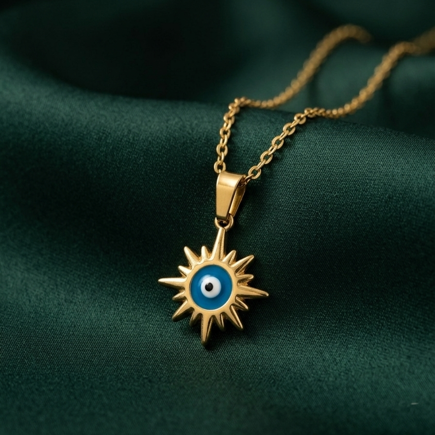 18k gold plated necklace featuring a radiant sunburst pendant with a classic blue and white enamel evil eye in the center on a green fabric background