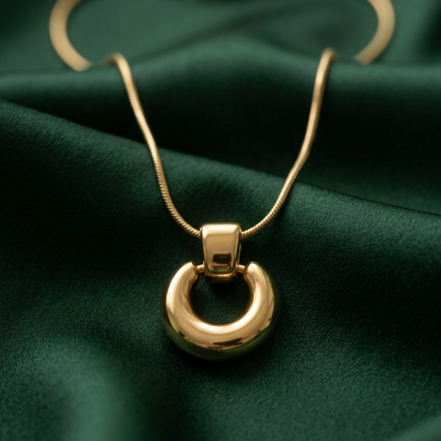 18k gold plated necklace featuring a thick, chunky donut-shaped hoop pendant suspended on a sleek snake chain on a green fabric background