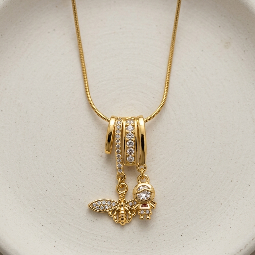 18k gold plated necklace featuring an intricate diamond-encrusted sliding bail holding a detailed golden bee charm and a small figure charm.
