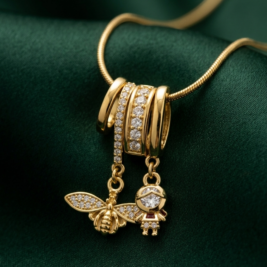 18k gold plated necklace featuring an intricate diamond-encrusted sliding bail holding a detailed golden bee charm and a small figure charm on a green fabric background