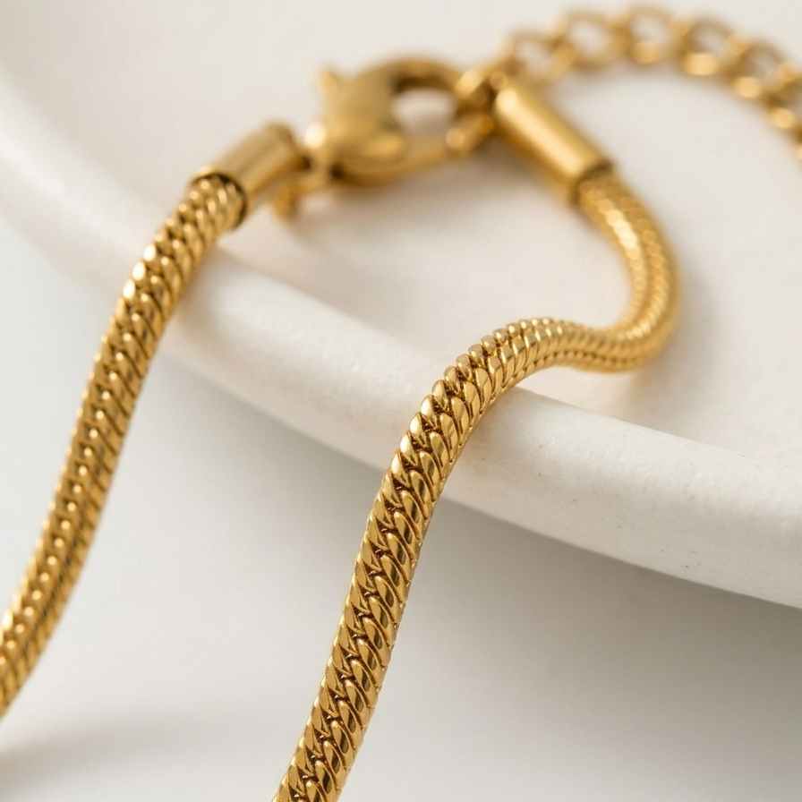 Extreme close up of an 18k gold plated foxtail layering chain showing intricate woven V-shaped links and an adjustable extender clasp.