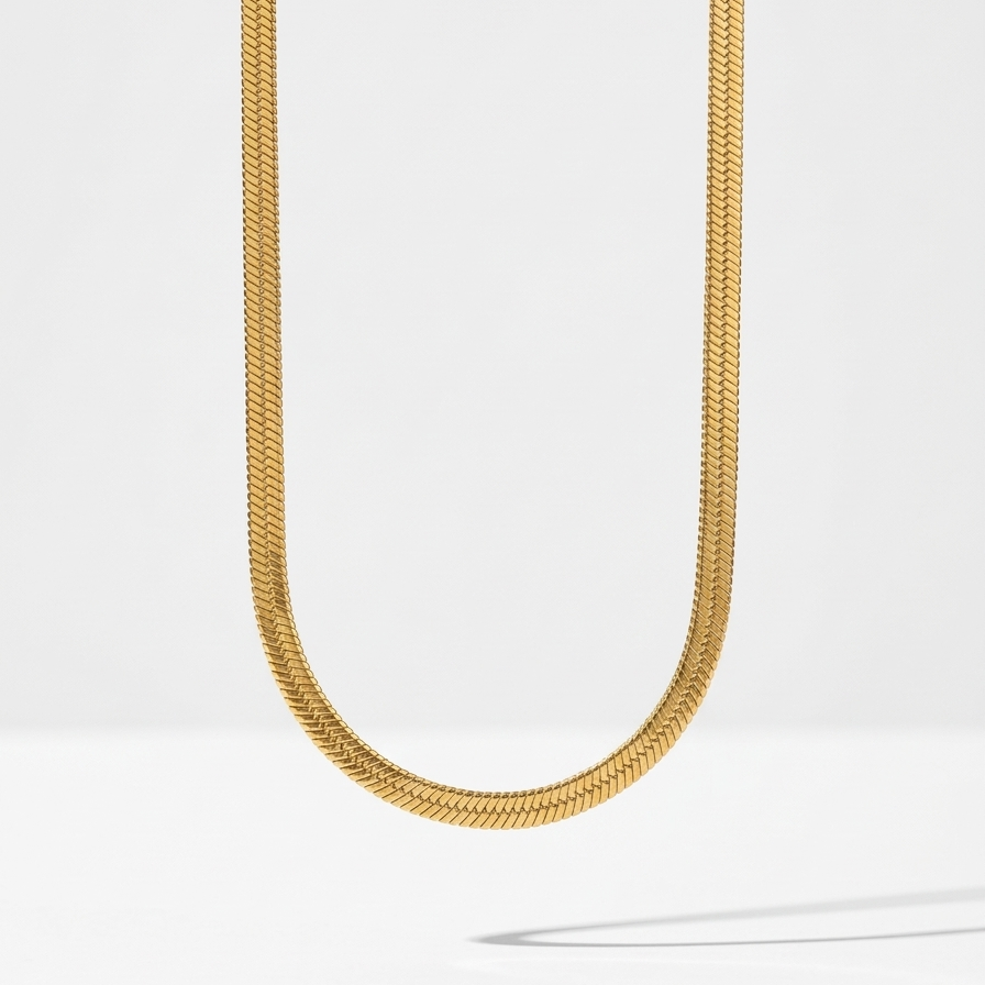 18k gold plated thick, flat herringbone chain necklace resting on a textured white surface.