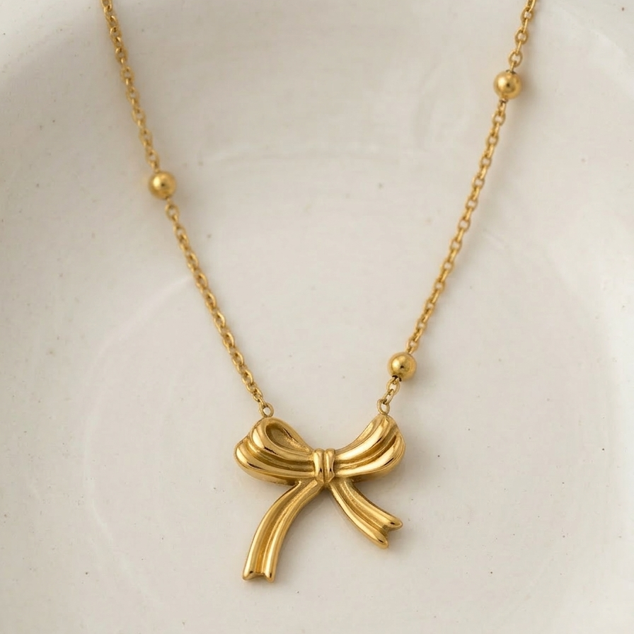 18k gold plated necklace featuring a sculpted, fluid ribbon bow pendant suspended on a delicate beaded satellite chain.