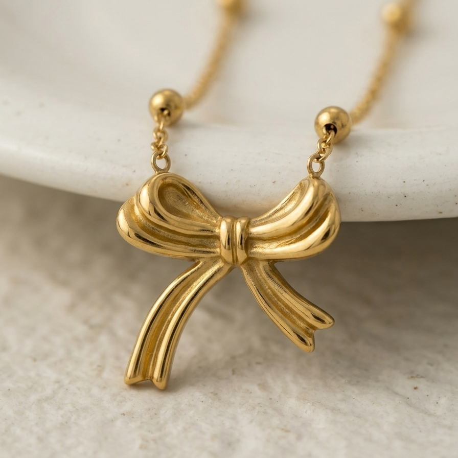 18k gold plated necklace featuring a sculpted, fluid ribbon bow pendant suspended on a delicate beaded satellite chain.