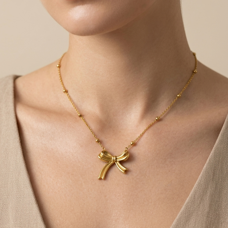18k gold plated necklace featuring a sculpted, fluid ribbon bow pendant suspended on a delicate beaded satellite chain.