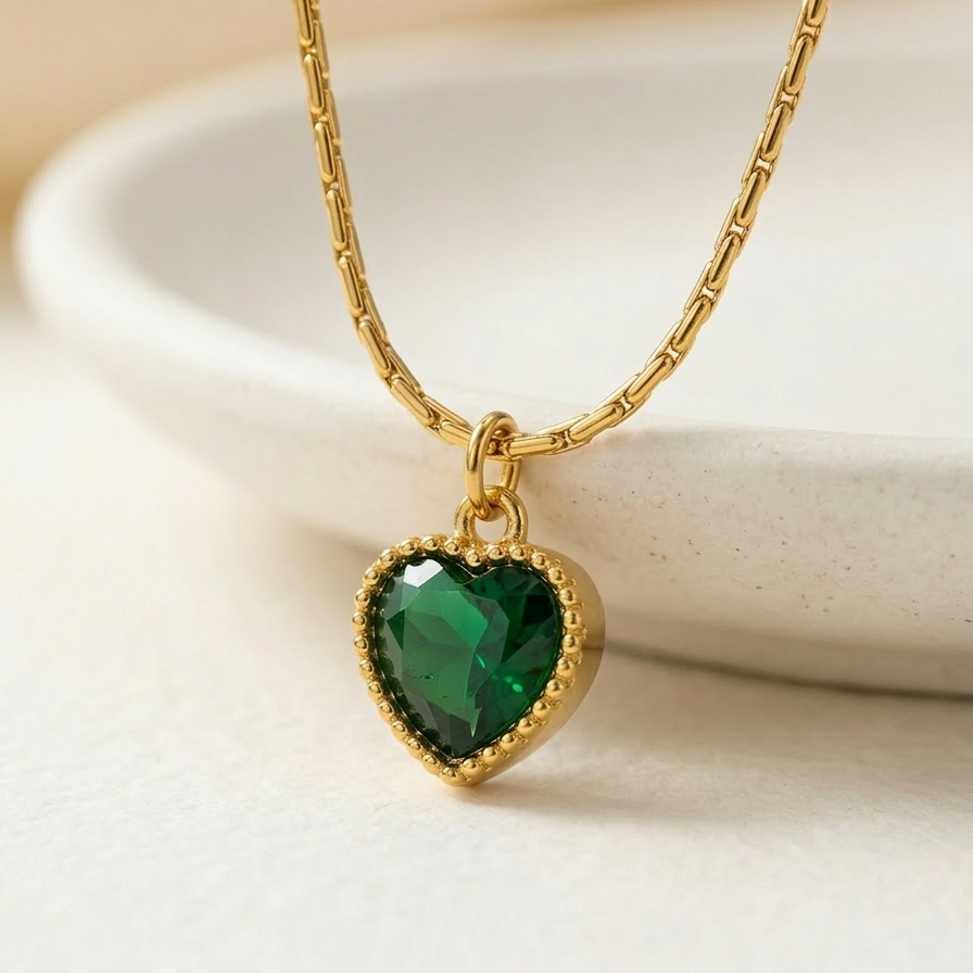 18k gold plated necklace featuring a deep emerald green heart-shaped crystal pendant with a textured golden border, on a delicate chain.