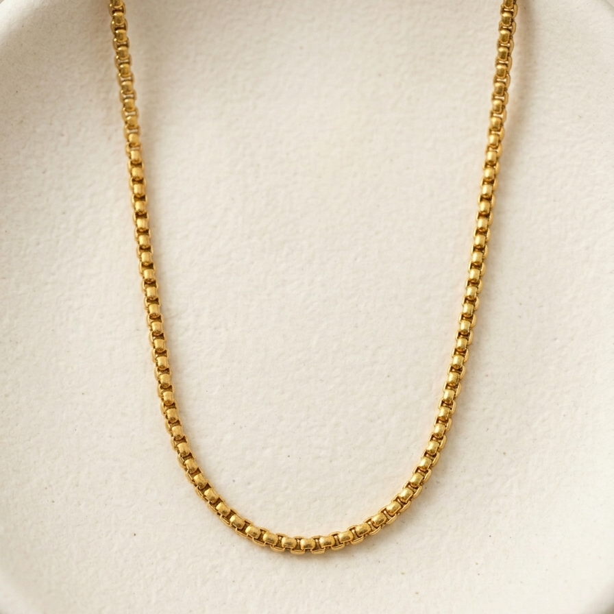 A gold beaded chain necklace draped over a textured white display stand.