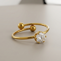 an 18k gold plated minimalist adjustable ring featuring a single CZ diamond and two small gold spheres, resting on a clean grey surface.