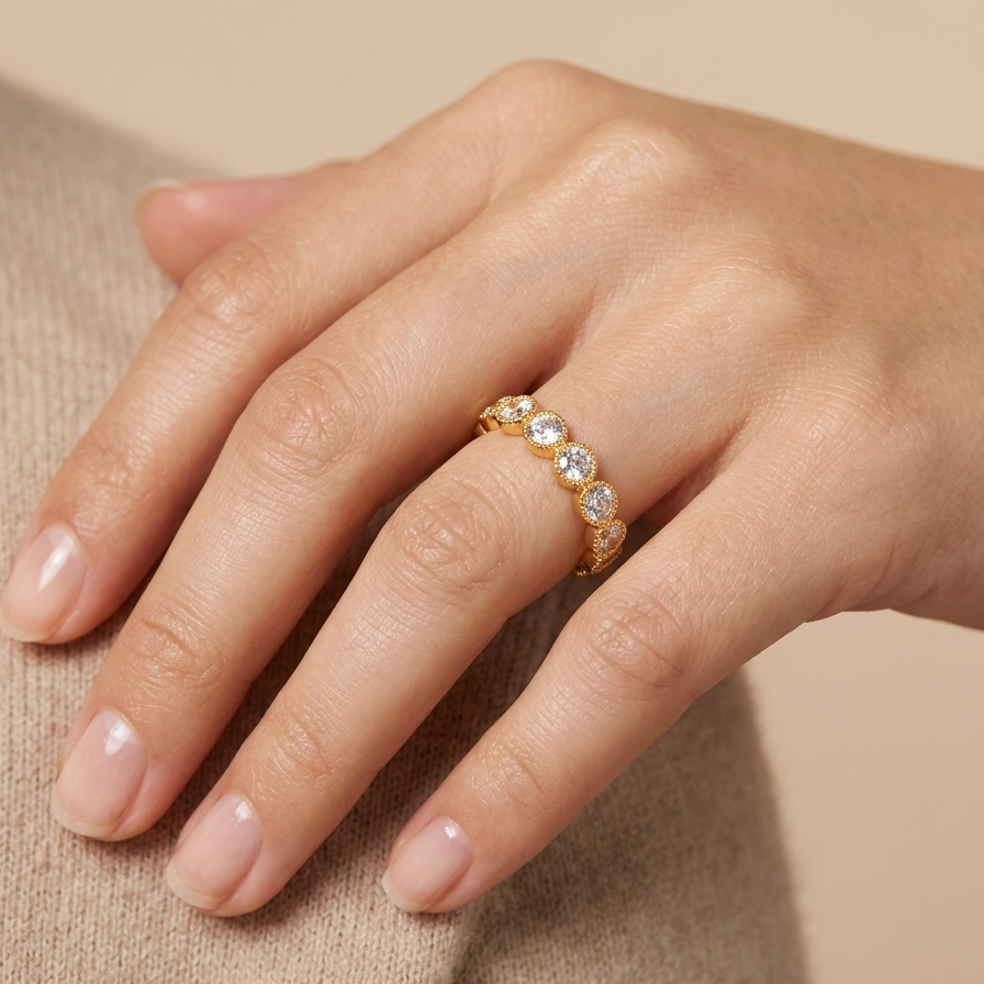 Close up of an 18k gold plated eternity band ring featuring a row of sparkling CZ diamonds with vintage beaded edges, wearing in a women's hand.