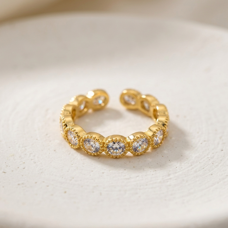 an 18k gold plated eternity band ring featuring a row of sparkling CZ diamonds with vintage beaded edges, resting on a textured white ceramic surface.