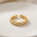 an 18k gold plated eternity band ring featuring a row of sparkling CZ diamonds with vintage beaded edges, resting on a textured white ceramic surface.