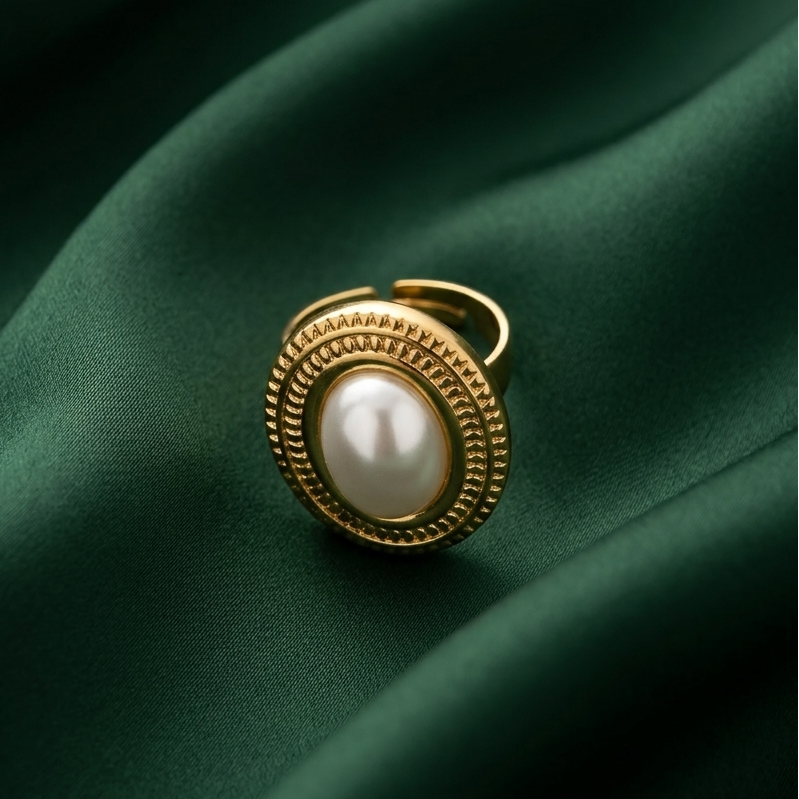 a premium 18k gold plated statement ring featuring a large oval pearl set in a detailed vintage bezel, resting on a deep green fabric.