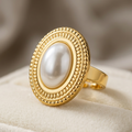Close up of a premium 18k gold plated statement ring featuring a large oval pearl set in a detailed vintage bezel, displayed on a cream velvet ring box.