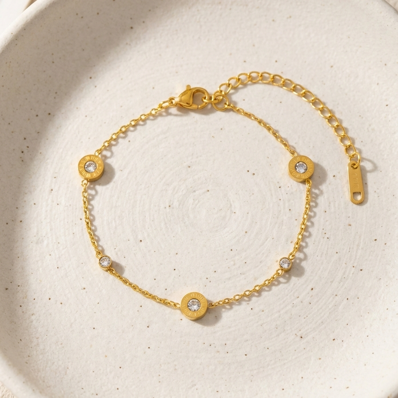 Gold chain bracelet with Roman numeral and crystal station charms on jewelry box.