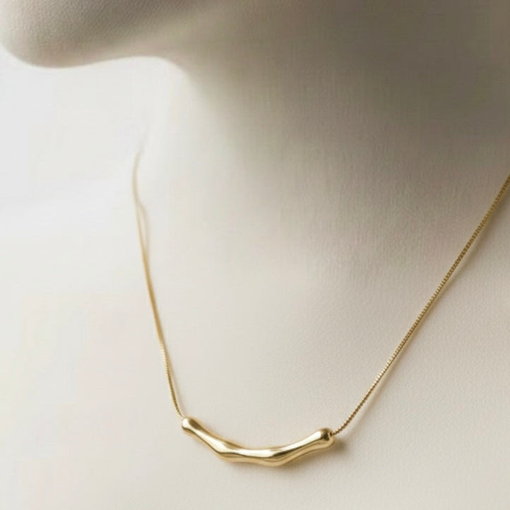 Gold necklace with curved bamboo texture bar sliding on a link chain on model neck.