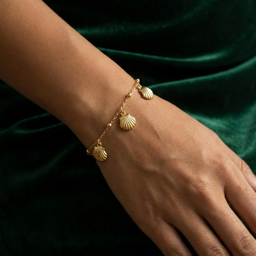 Gold chain bracelet with five dangling scallop shell charms on white packaging.