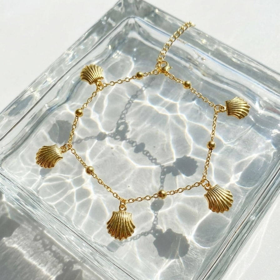 Gold chain bracelet with five dangling scallop shell charms on white packaging.