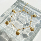 Gold chain bracelet with five dangling scallop shell charms on white packaging.