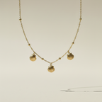 Gold shell charm necklace with three scallop shells on beaded chain white background.