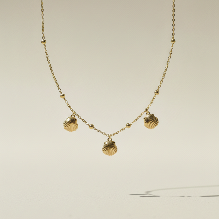 Gold shell charm necklace with three scallop shells on beaded chain white background.