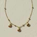 Gold shell charm necklace with three scallop shells on beaded chain white background.