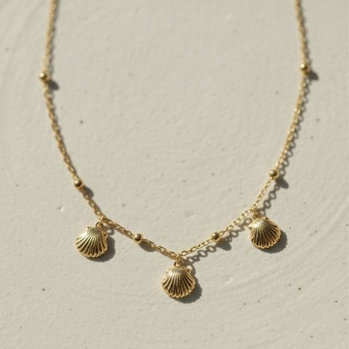 Gold shell charm necklace with three scallop shells on beaded chain white background.