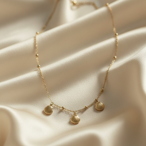Gold shell charm necklace with three scallop shells on beaded chain white background.