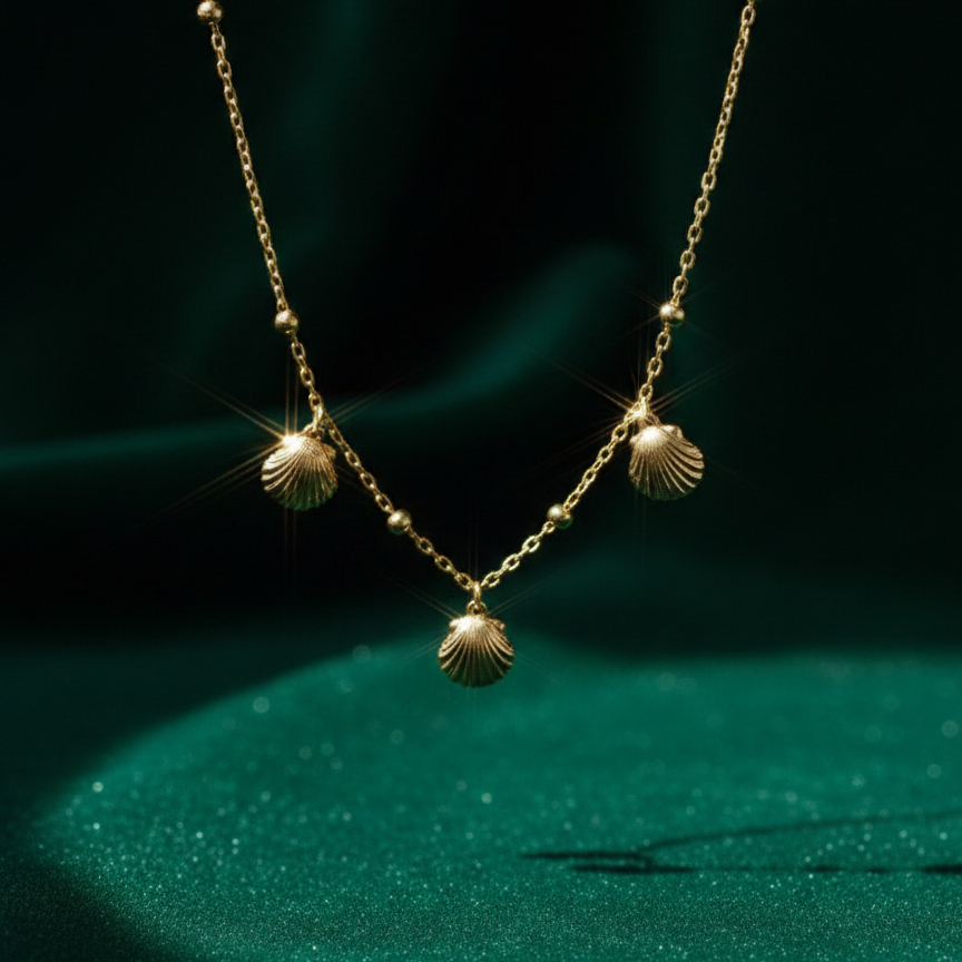 Gold shell charm necklace with three scallop shells on beaded chain white background.