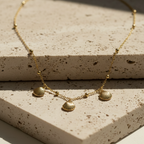Gold shell charm necklace with three scallop shells on beaded chain white background.
