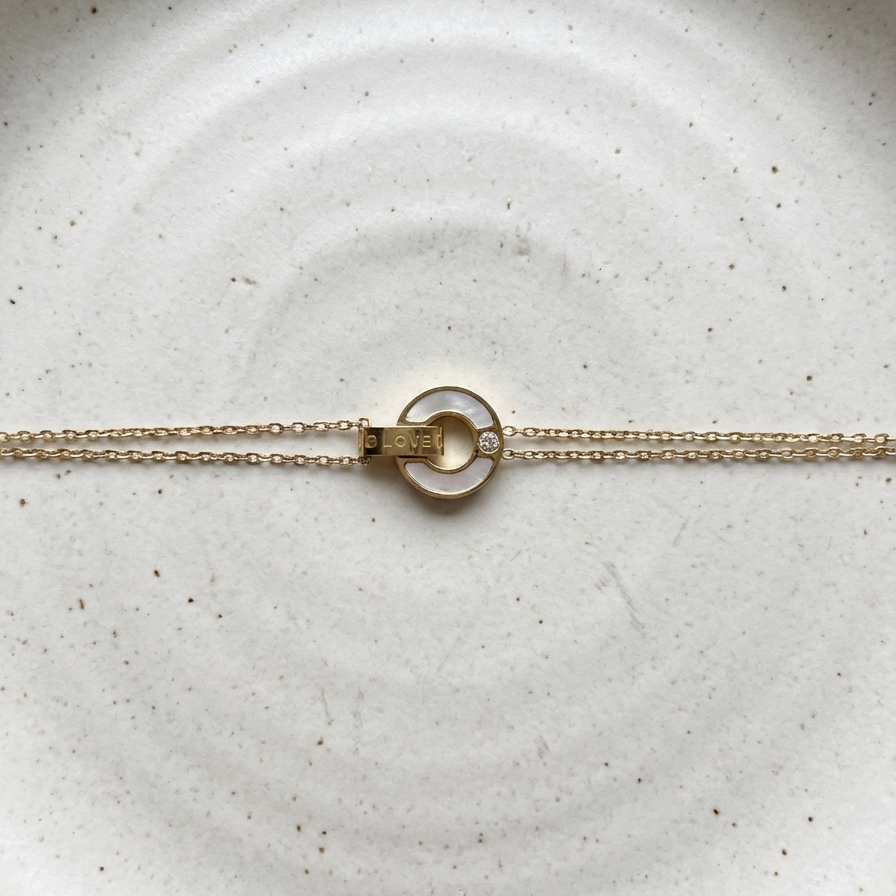 Gold chain bracelet with interlocking circles, mother of pearl inlay and engraved LOVE text on stone background.