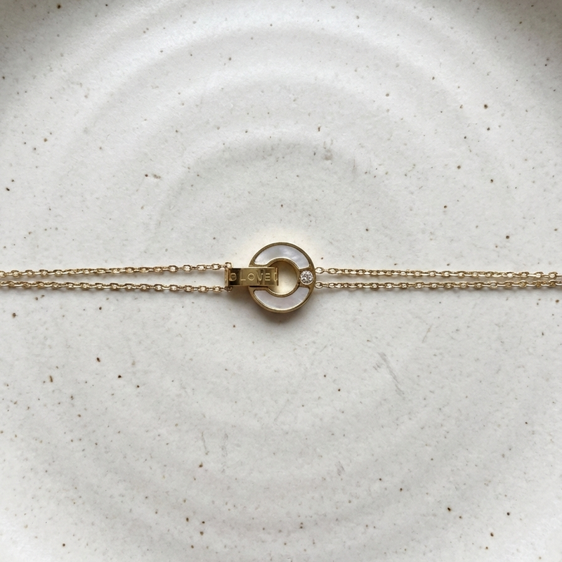 Gold chain bracelet with interlocking circles, mother of pearl inlay and engraved LOVE text on stone background.