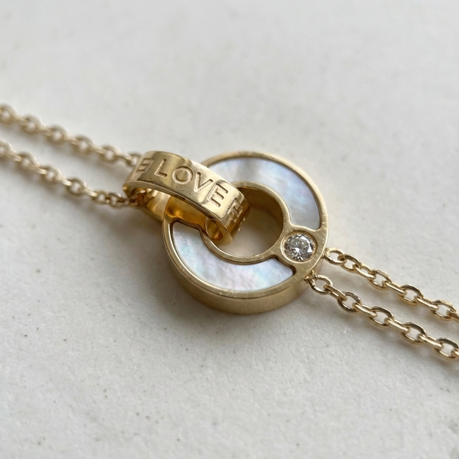 Gold chain bracelet with interlocking circles, mother of pearl inlay and engraved LOVE text on stone background.