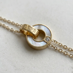 Gold chain bracelet with interlocking circles, mother of pearl inlay and engraved LOVE text on stone background.