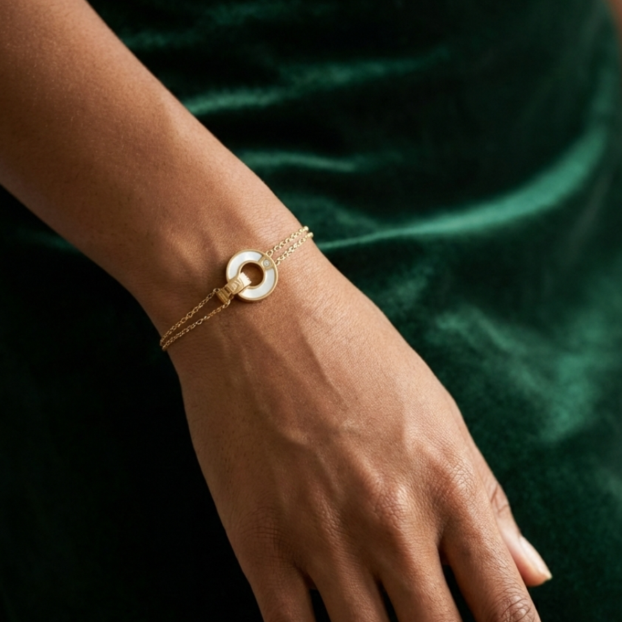 Gold chain bracelet with interlocking circles, mother of pearl inlay and engraved LOVE text on stone background.