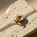 Gold chain bracelet with interlocking circles, mother of pearl inlay and engraved LOVE text on stone background.