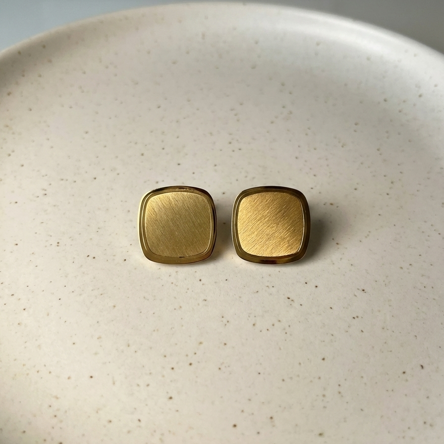 Square gold stud earrings with matte brushed texture and polished rim on white surface.