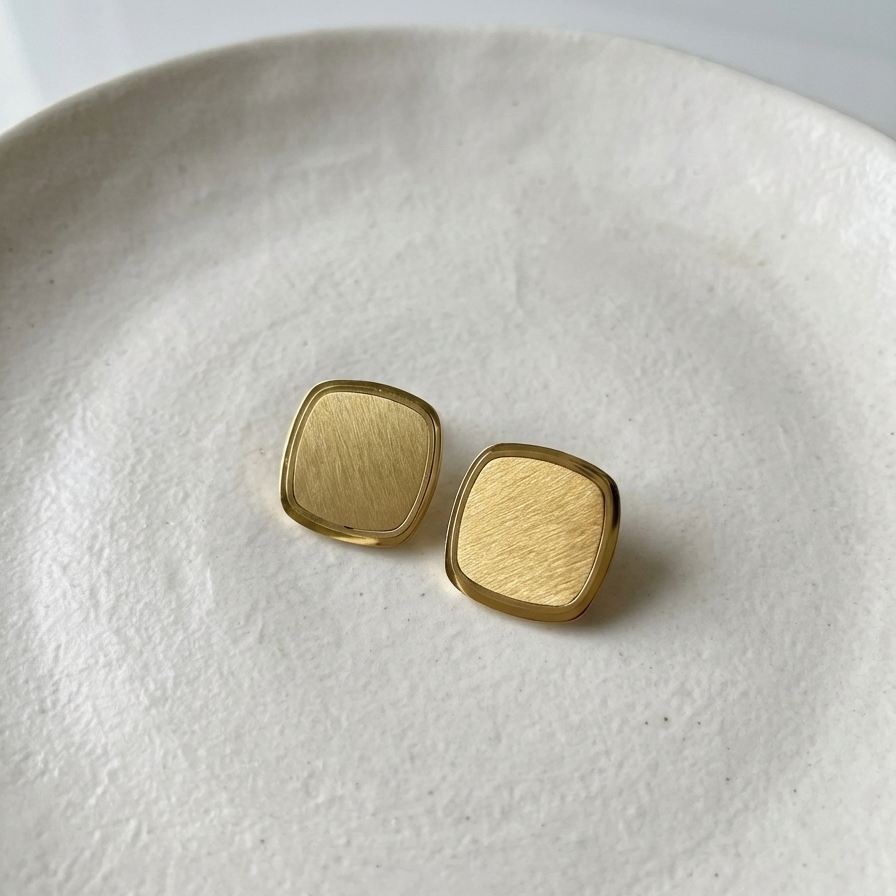 Square gold stud earrings with matte brushed texture and polished rim on white surface.