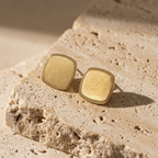 Square gold stud earrings with matte brushed texture and polished rim on white surface.