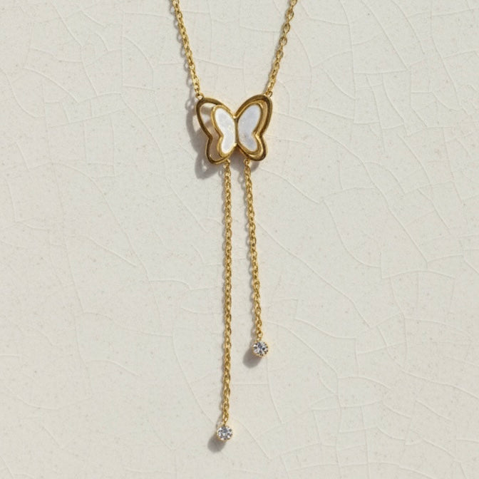 Gold butterfly necklace with dangling tassels and white inlay on packaging card.