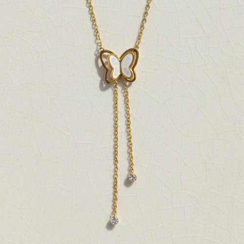 Gold butterfly necklace with dangling tassels and white inlay on packaging card.