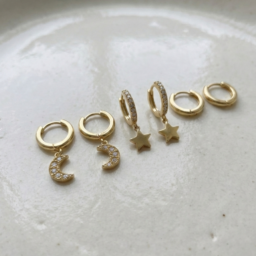 Set of gold huggie earrings with dangling star and moon charms on packaging card.