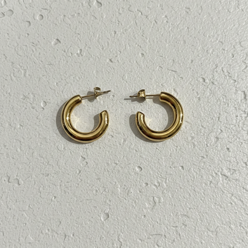 Pair of chunky gold tube hoop earrings on white background.
