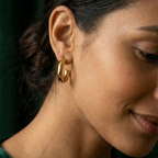 Pair of chunky gold tube hoop earrings on white background.