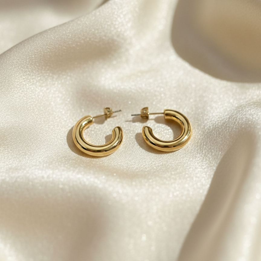 Pair of chunky gold tube hoop earrings on white background.