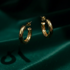 Pair of chunky gold tube hoop earrings on white background.