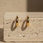 Pair of chunky gold tube hoop earrings on white background.