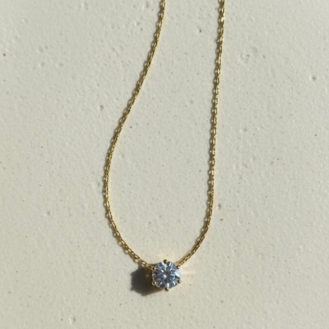 Single round crystal solitaire pendant necklace on white fabric background.