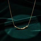 Gold necklace with curved bamboo texture bar sliding on a link chain on model neck.